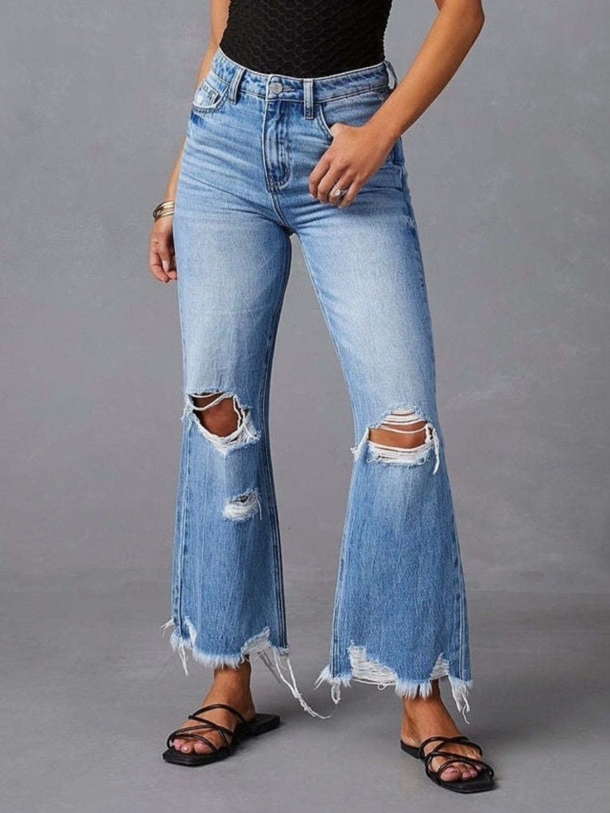 Full-length front view of light-wash flare jeans with distressed knees and frayed hems.