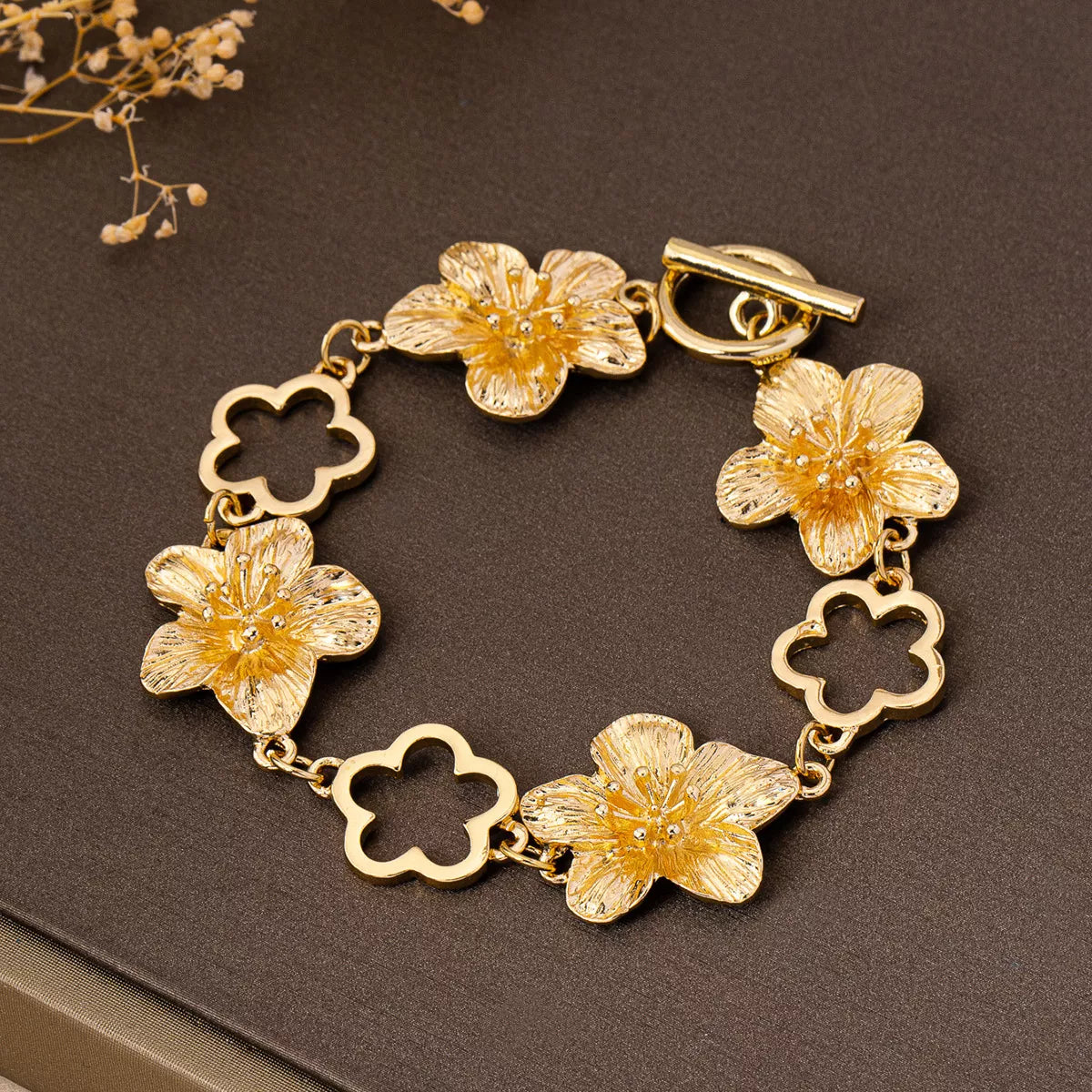 Gold-tone flower bracelet with open flower-shaped links on dark background