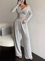 Mirror view of light grey button-detail long-sleeve top and wide-leg pants with one hand in a pocket