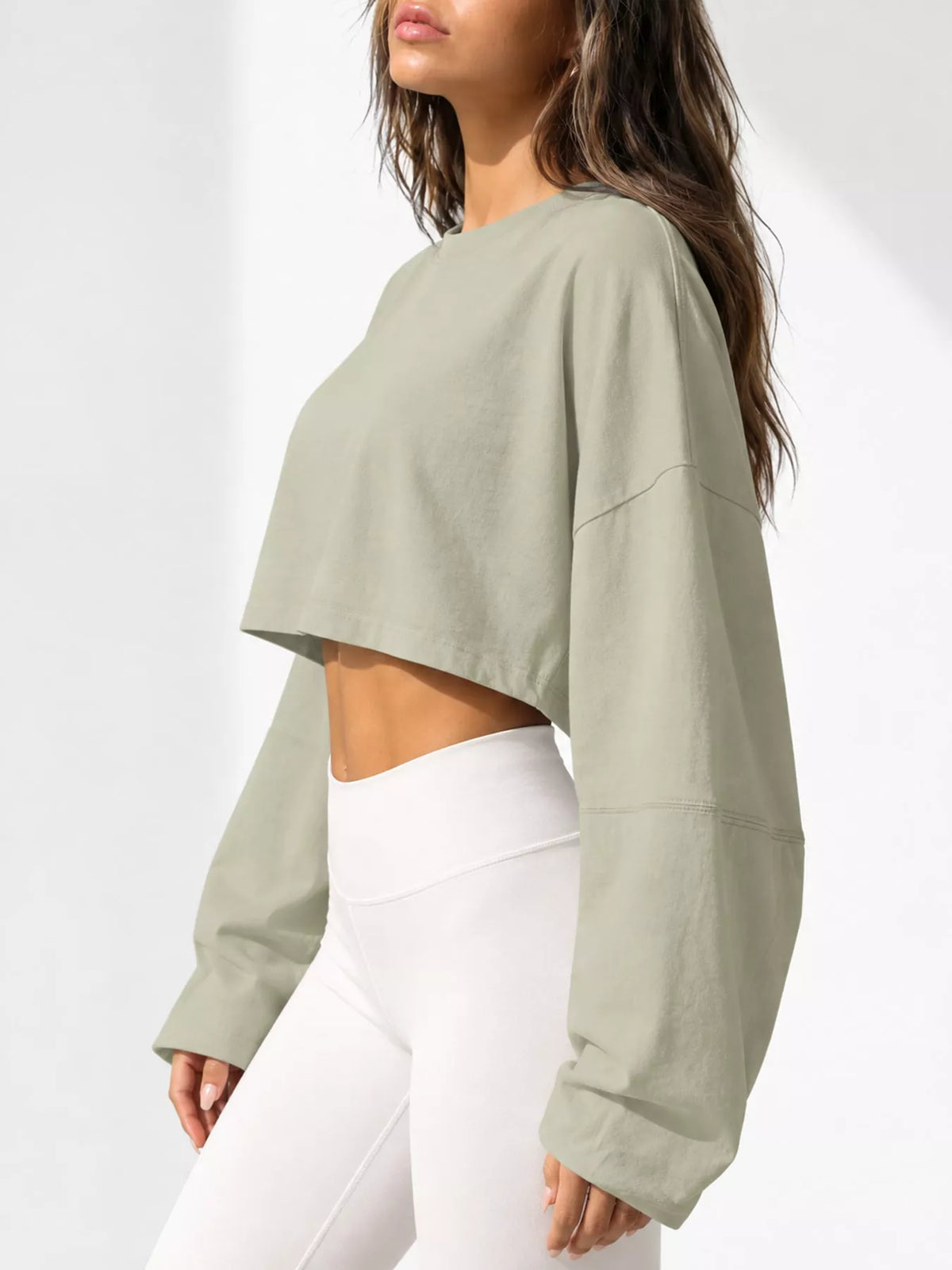 Side view of a pale sage cropped sweatshirt with long sleeves, worn with white leggings.