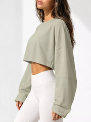 Side view of a pale sage cropped sweatshirt with long sleeves, worn with white leggings.