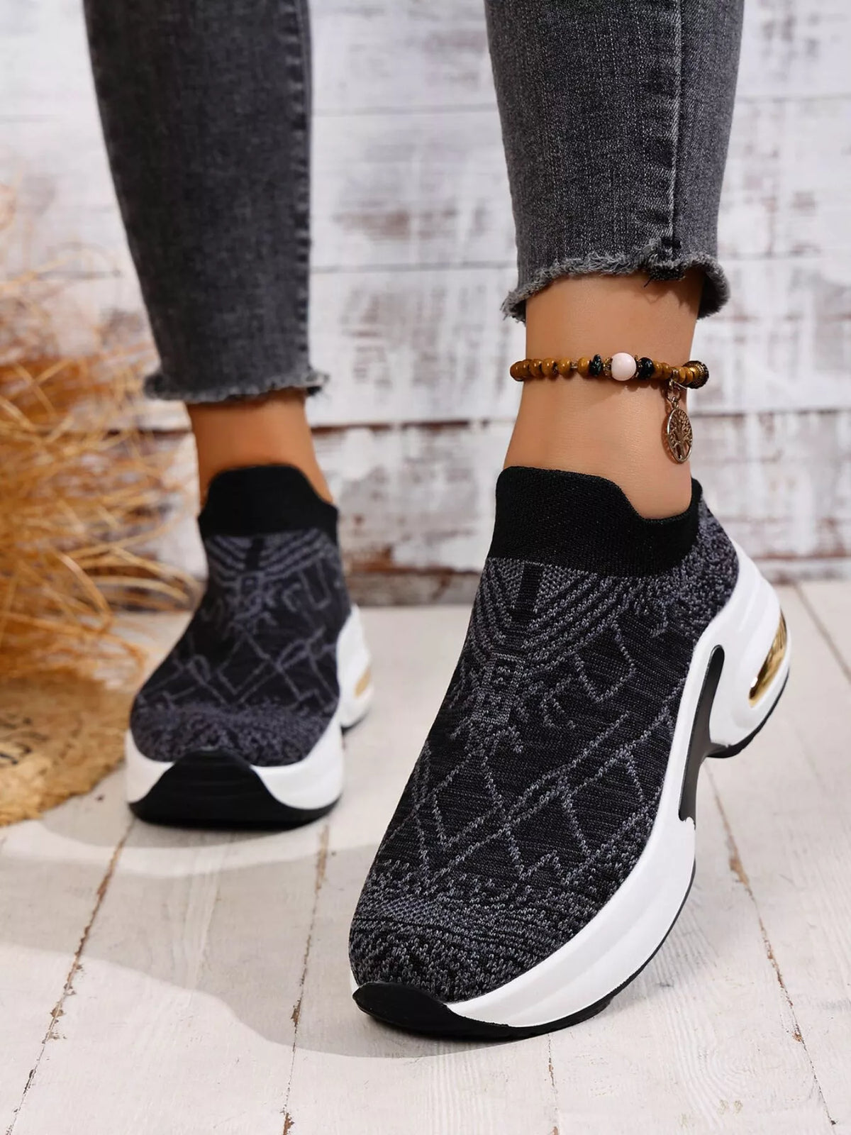 Angled view of black patterned slip-on trainers showing the gold-coloured heel accent