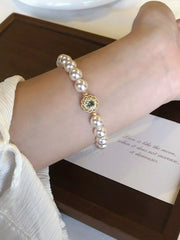 Wrist view of a pearl bracelet with a green-centered gold flower charm