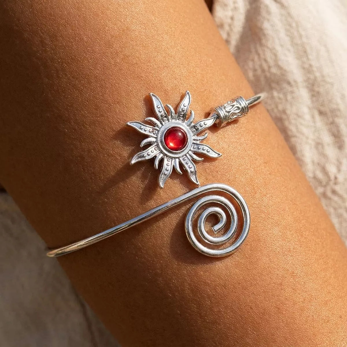 Silver-tone sunburst cuff bracelet with red center worn on a wrist
