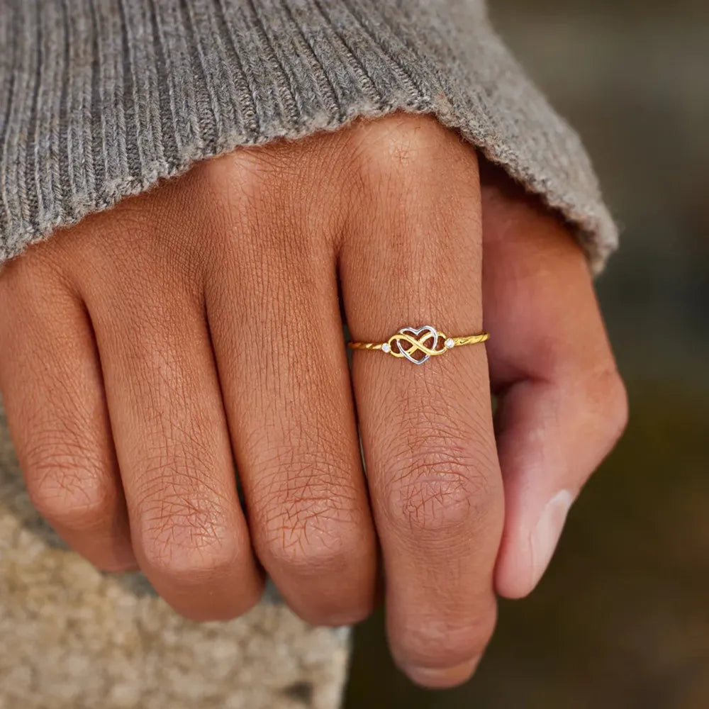 Gold infinity-heart ring worn on a hand in a gray sweater