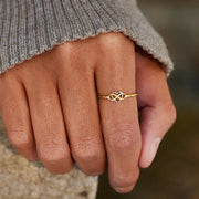 Gold infinity-heart ring worn on a hand in a gray sweater