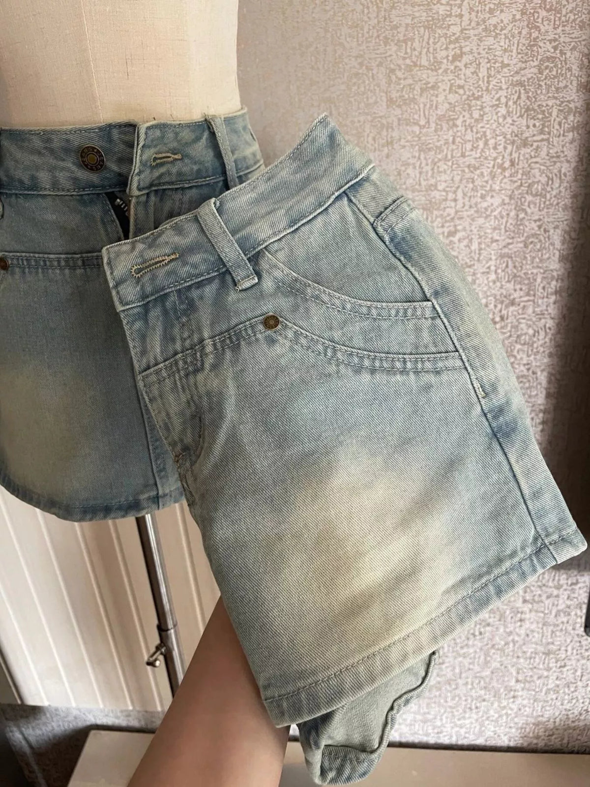 Close-up of waistband and front pocket on light-wash denim shorts