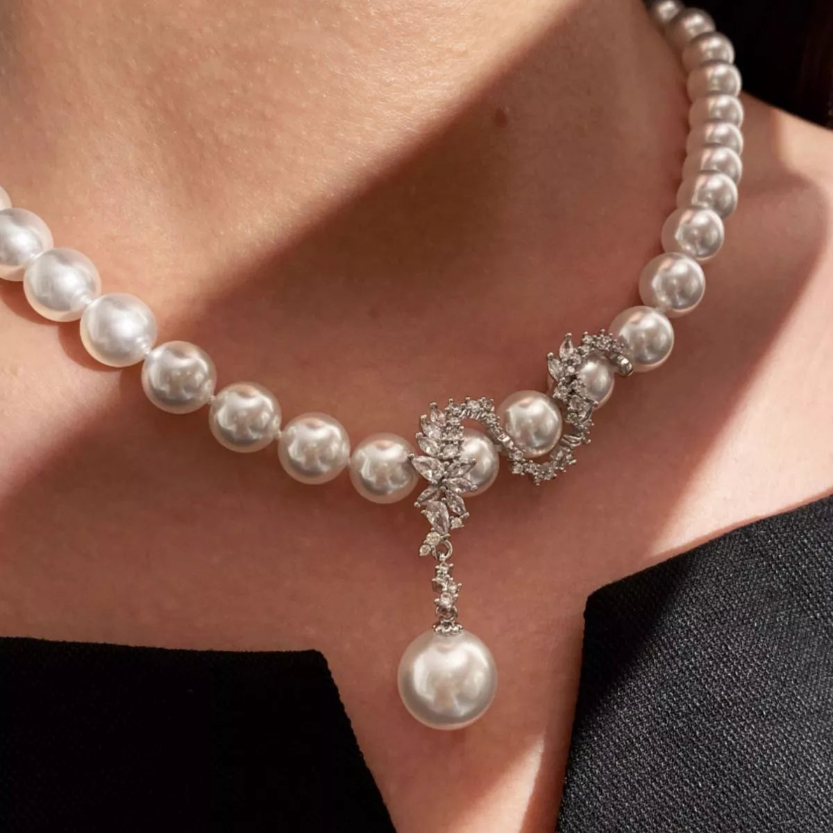 Pearl necklace with sparkling floral zircon centerpiece and dangling pearl drop, worn close-up