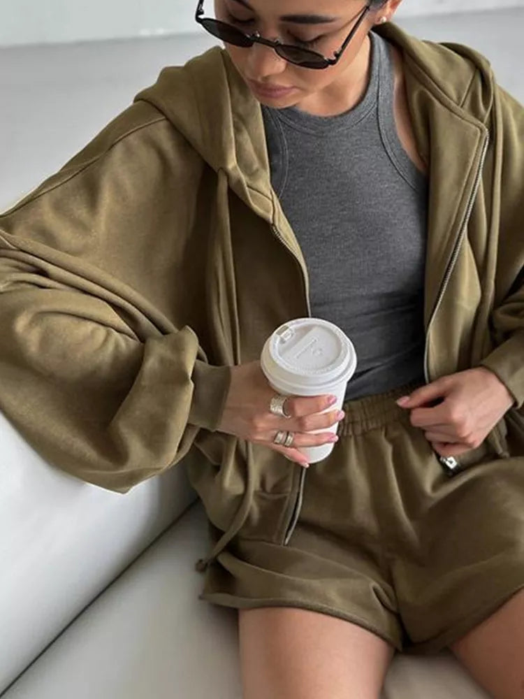 Seated model in olive hoodie and shorts holding a cup