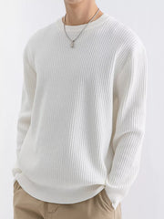 Angled view of a model in an ivory ribbed crew-neck sweater with one hand in a trouser pocket