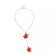 Gold-tone pearl necklace with two red flower pendants laid flat