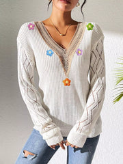 White floral-appliqué sweater shown from the front with hands clasped at the hem.