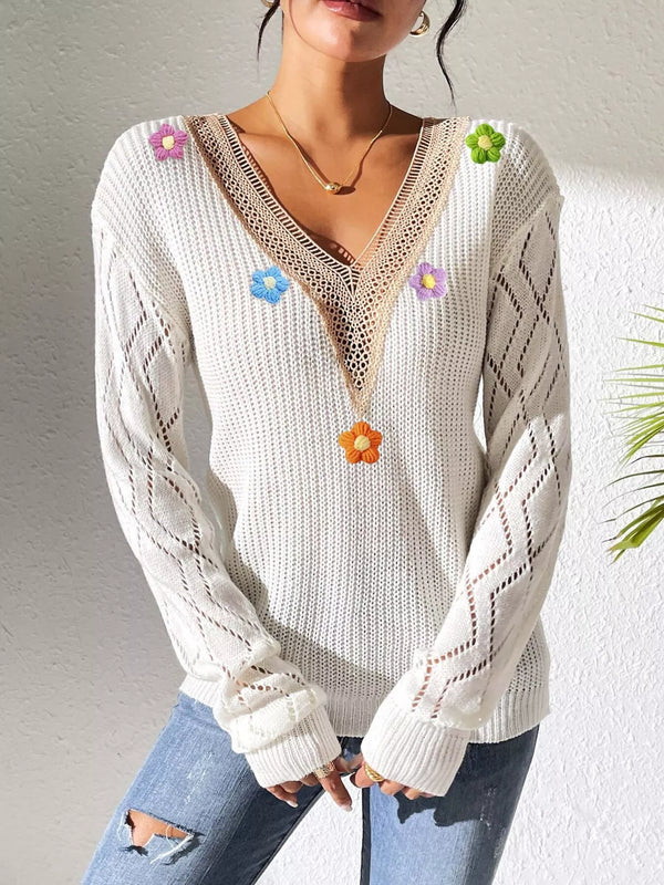 White floral-appliqué sweater shown from the front with hands clasped at the hem.