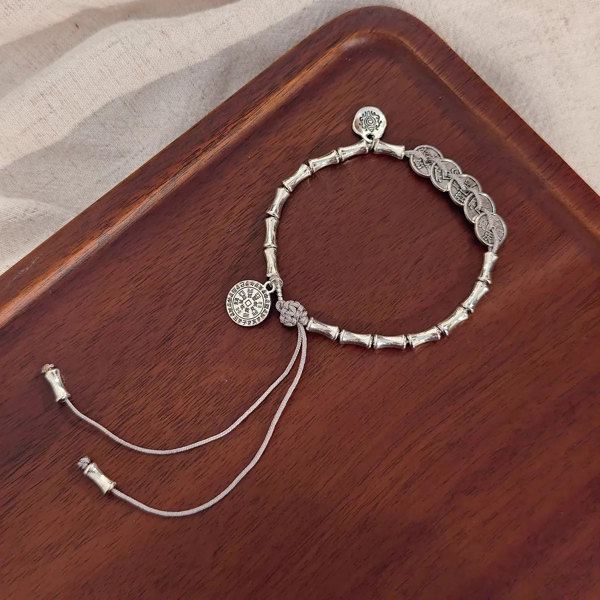 Silver-tone charm bracelet arranged on a wooden tray with its two long adjustment chains extended.