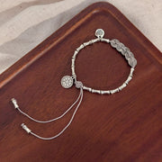 Silver-tone charm bracelet arranged on a wooden tray with its two long adjustment chains extended.