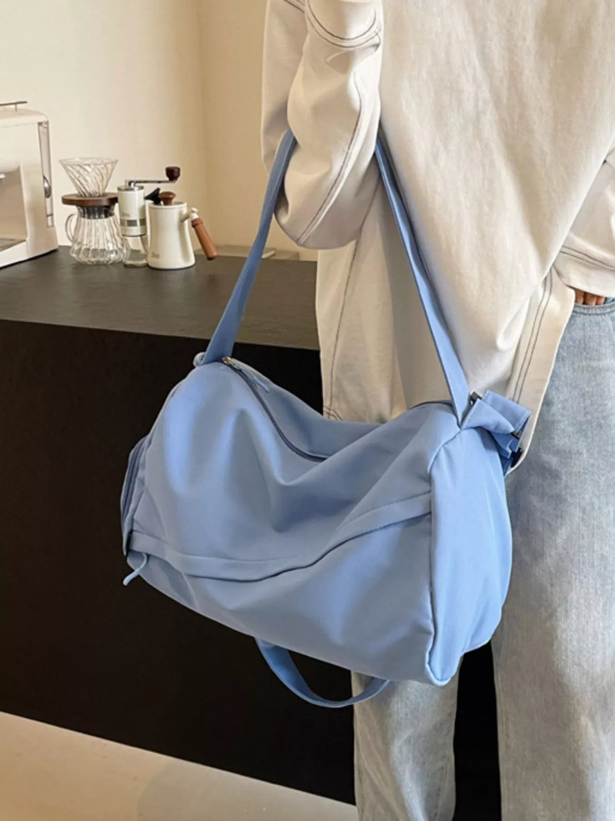 Blue duffel bag worn crossbody on a long shoulder strap, rear side view