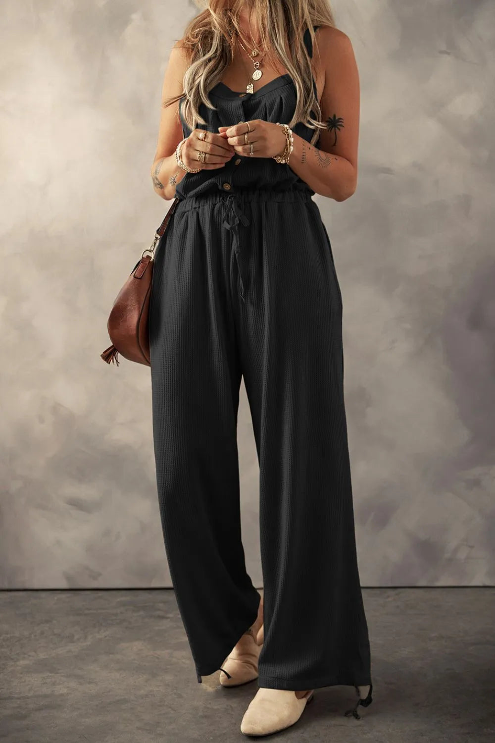 Black textured jumpsuit with knotted straps, model front view holding phone