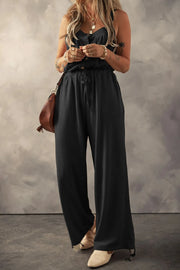 Black textured jumpsuit with knotted straps, model front view holding phone
