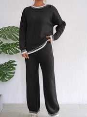 Black knit set shown standing with one hand at the hip and the sweater hem angled.
