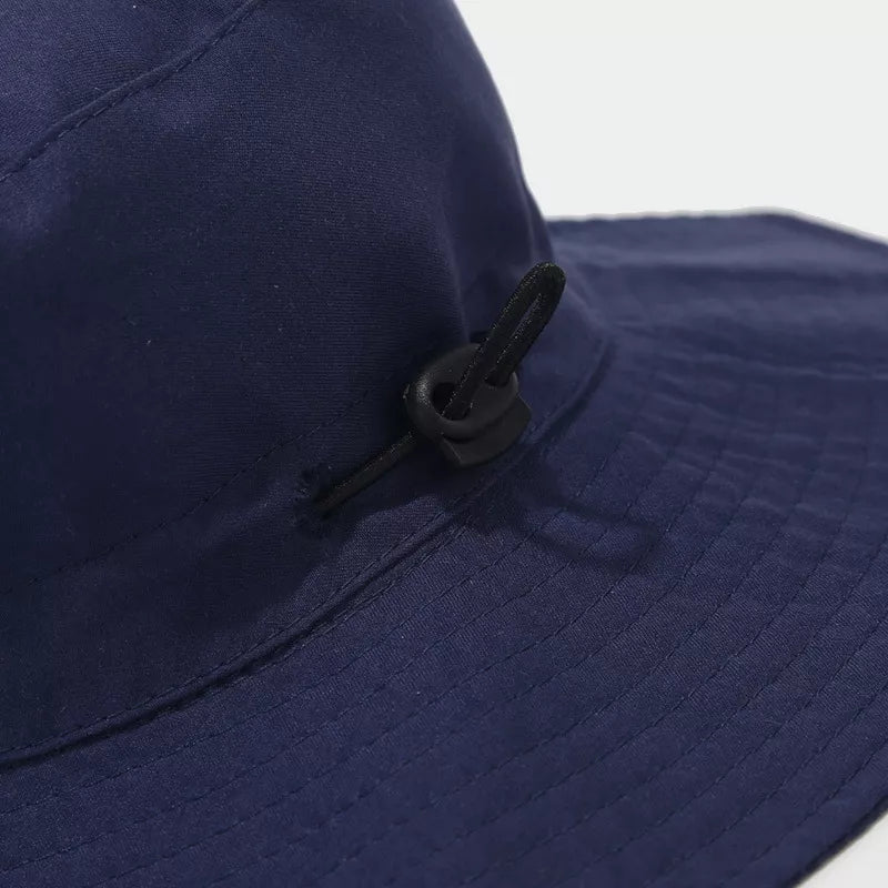Close-up of the navy hat's side cord toggle and stitched brim.