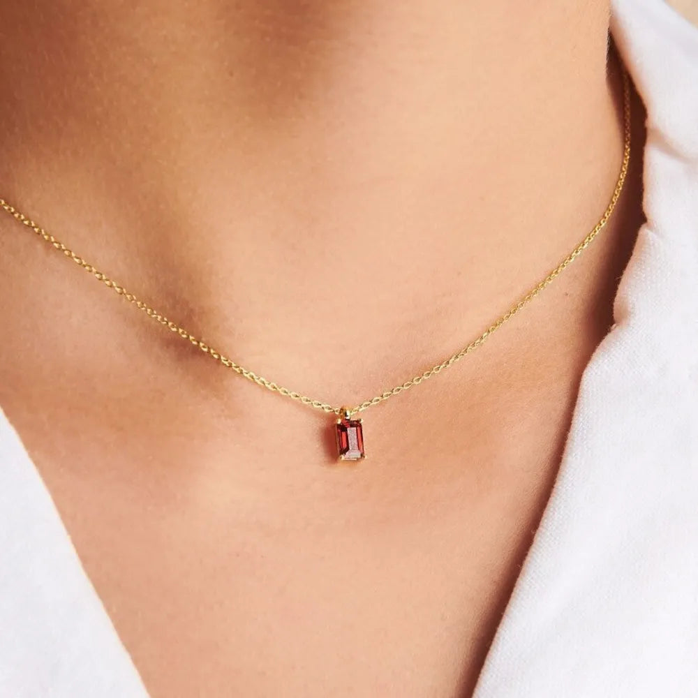 Gold-tone necklace with a small red rectangular pendant worn with a white shirt