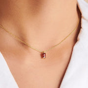 Gold-tone necklace with a small red rectangular pendant worn with a white shirt