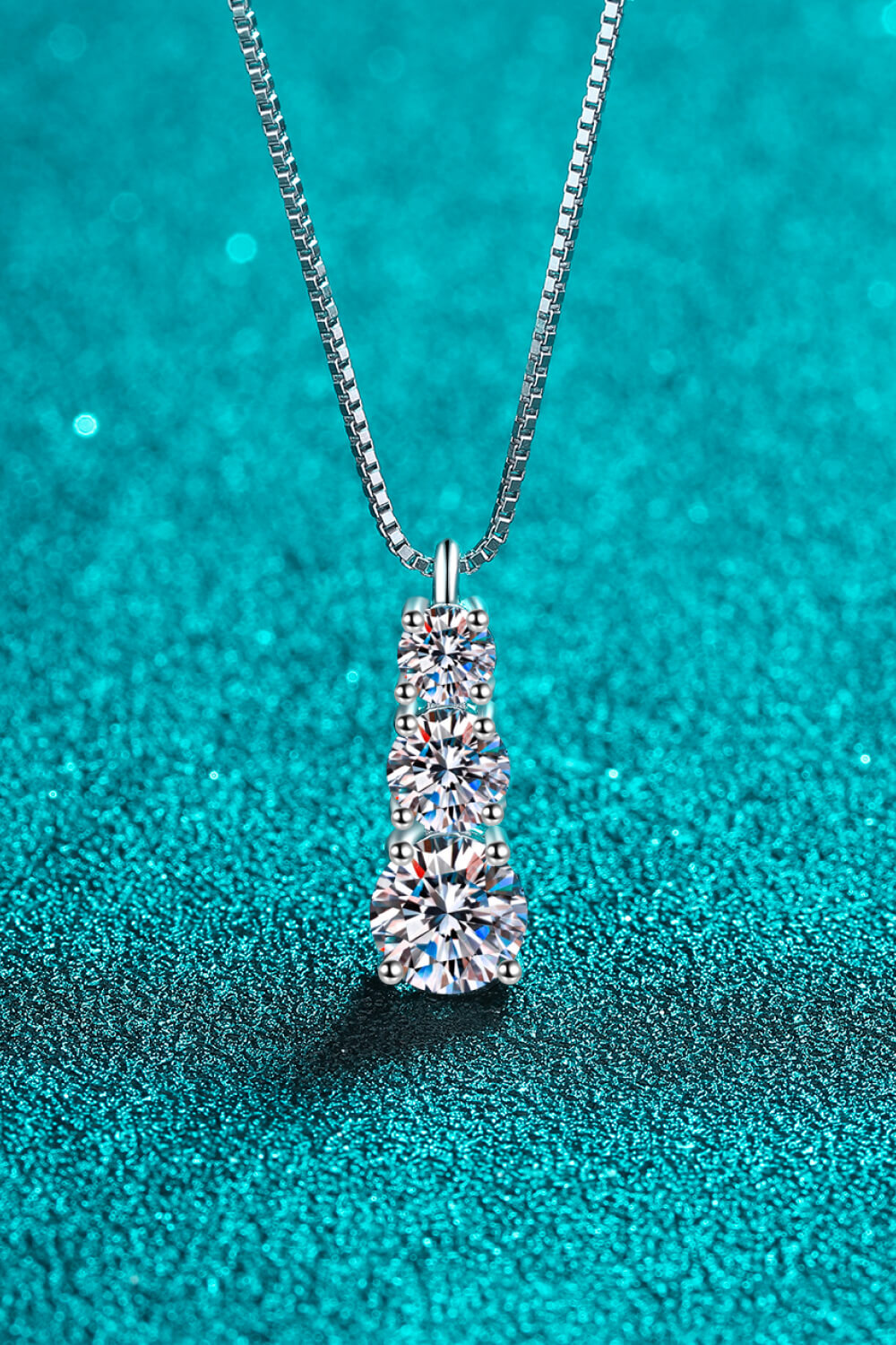 Three-stone pendant necklace displayed against teal fabric