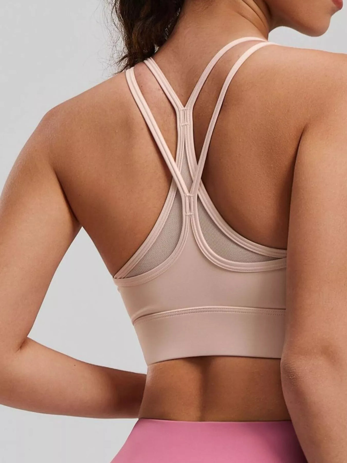 Close-up of pale pink active bra showing crossed back straps and mesh inset