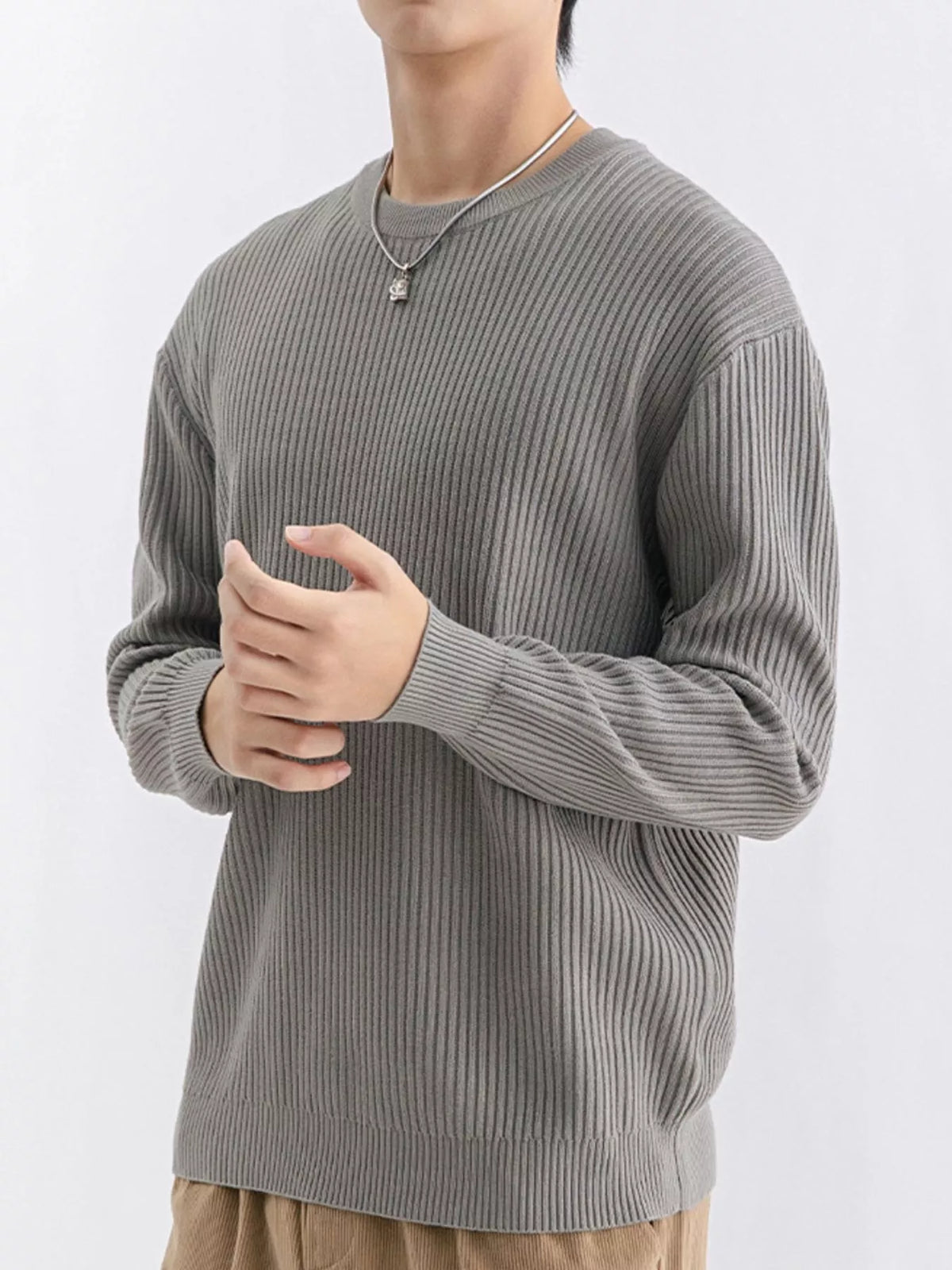 Angled view of medium grey crew-neck sweater with the model's hands held together