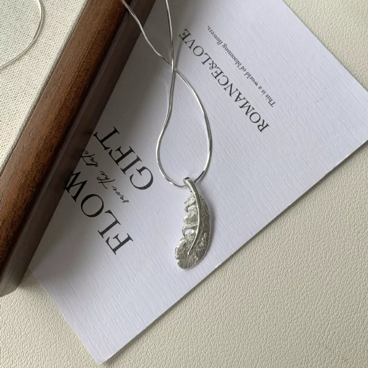 Silver feather pendant necklace displayed on a jewelry card