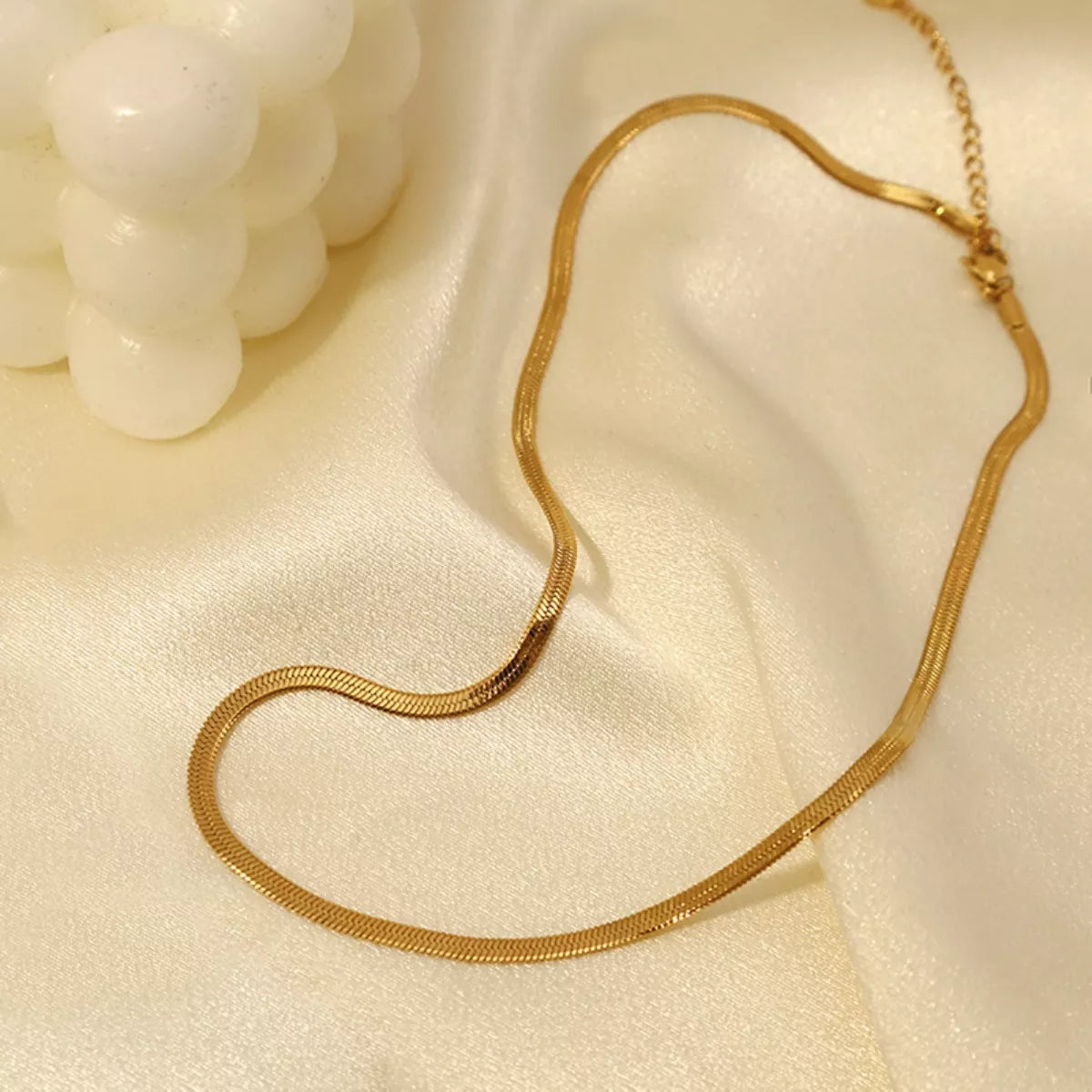 Gold-tone necklace displayed beside a small cream decorative ornament