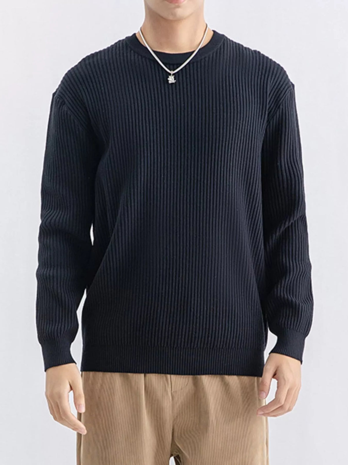 Model facing forward in a dark navy ribbed crew-neck sweater and tan trousers