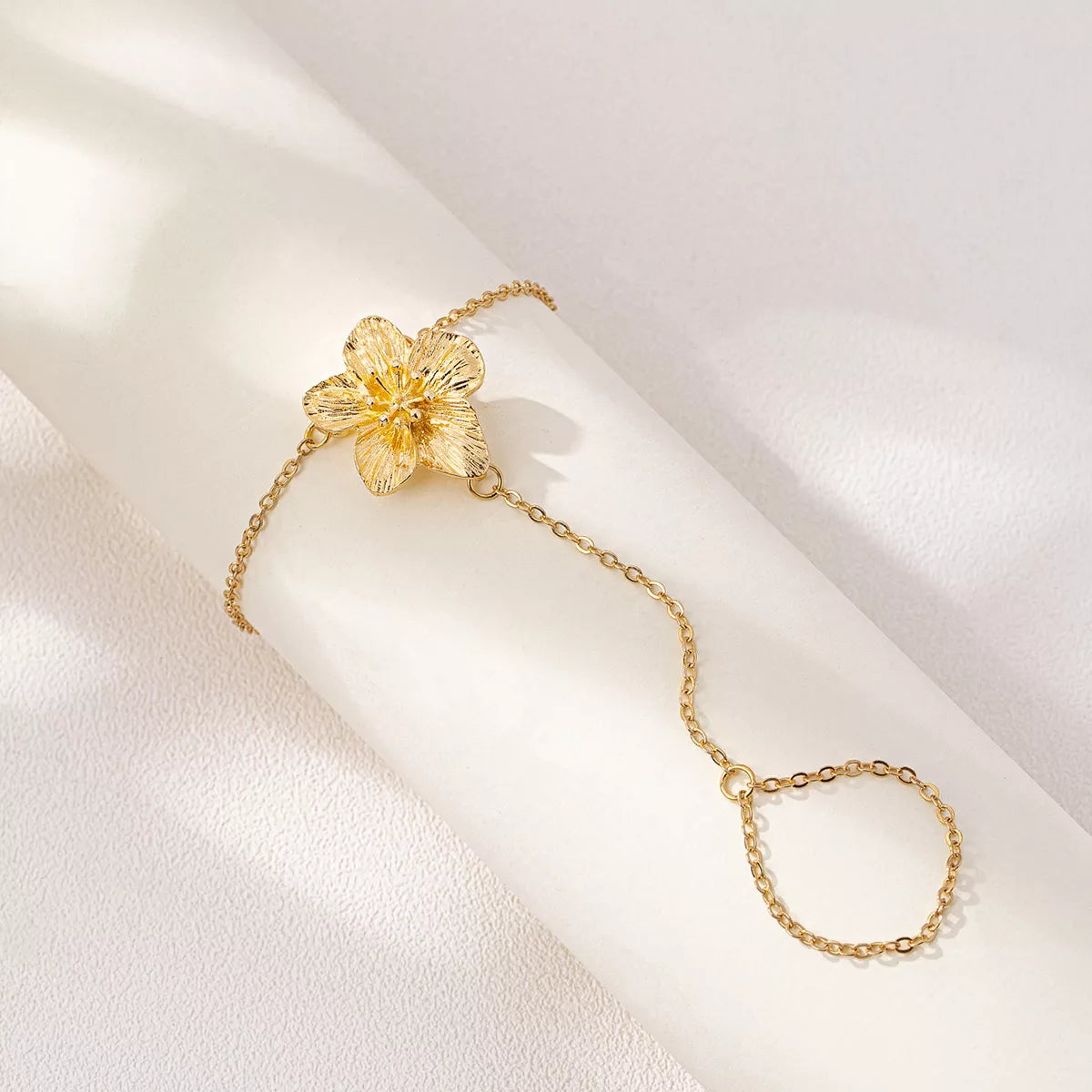 Gold-tone flower hand chain bracelet with finger loop on pale background
