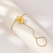 Gold-tone flower hand chain bracelet with finger loop on pale background