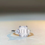 Clear emerald-cut center stone ring photographed at a distance on a light surface