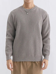 Model facing forward in a taupe ribbed crew-neck sweater and tan trousers