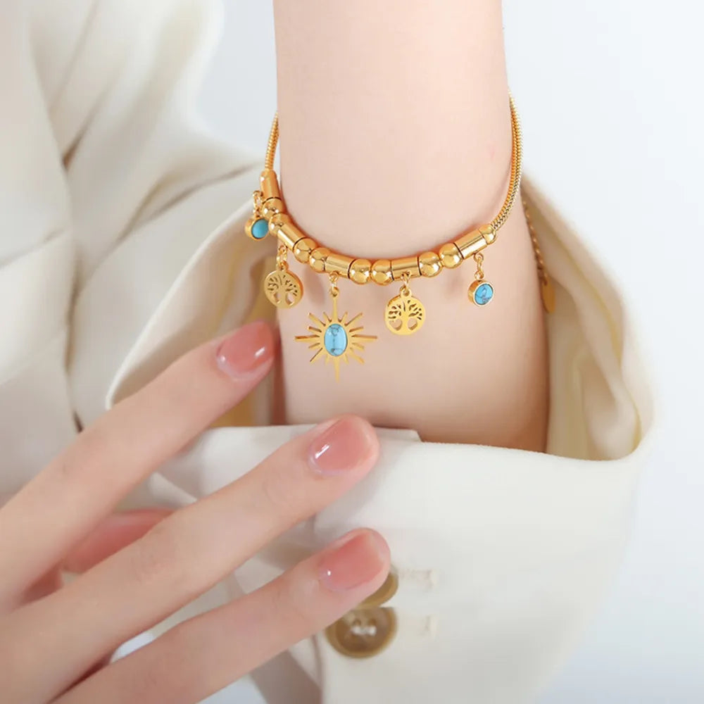 Gold charm bracelet with sun and blue accents worn on wrist