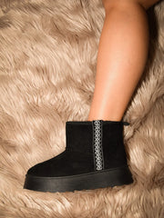 Black round-toe platform ankle boot worn with bare legs on a textured rug