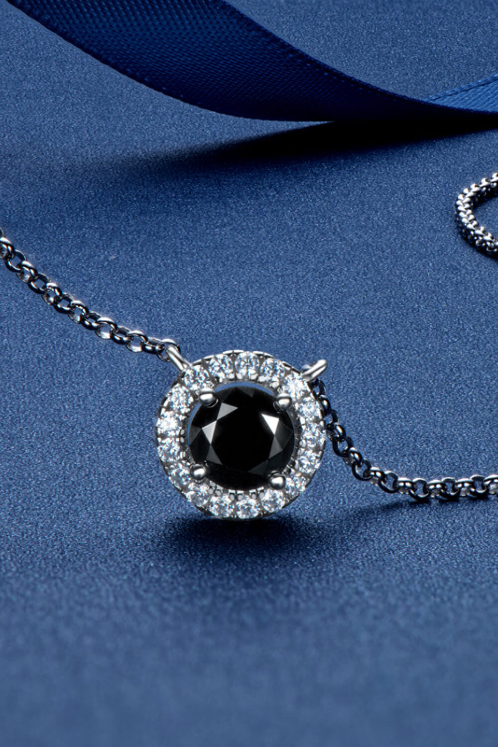 Round black-stone pendant with a clear halo and silver-tone chain on a blue surface