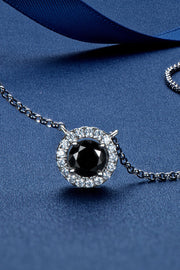 Round black-stone pendant with a clear halo and silver-tone chain on a blue surface