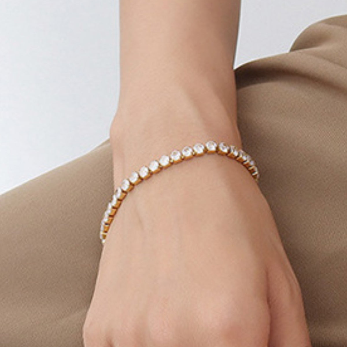 Gold-tone clear-stone tennis bracelet worn around the wrist