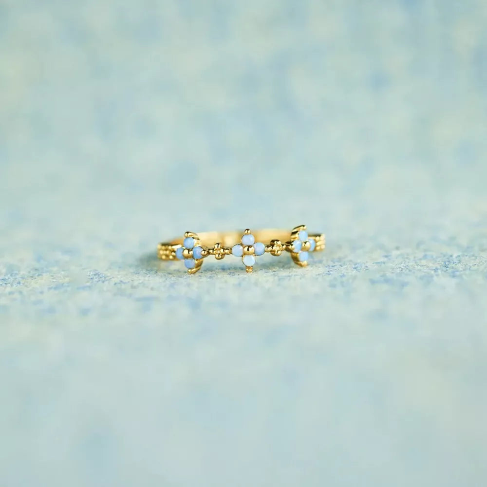 Gold-tone sterling silver flower ring with blue and clear stones on pale fabric