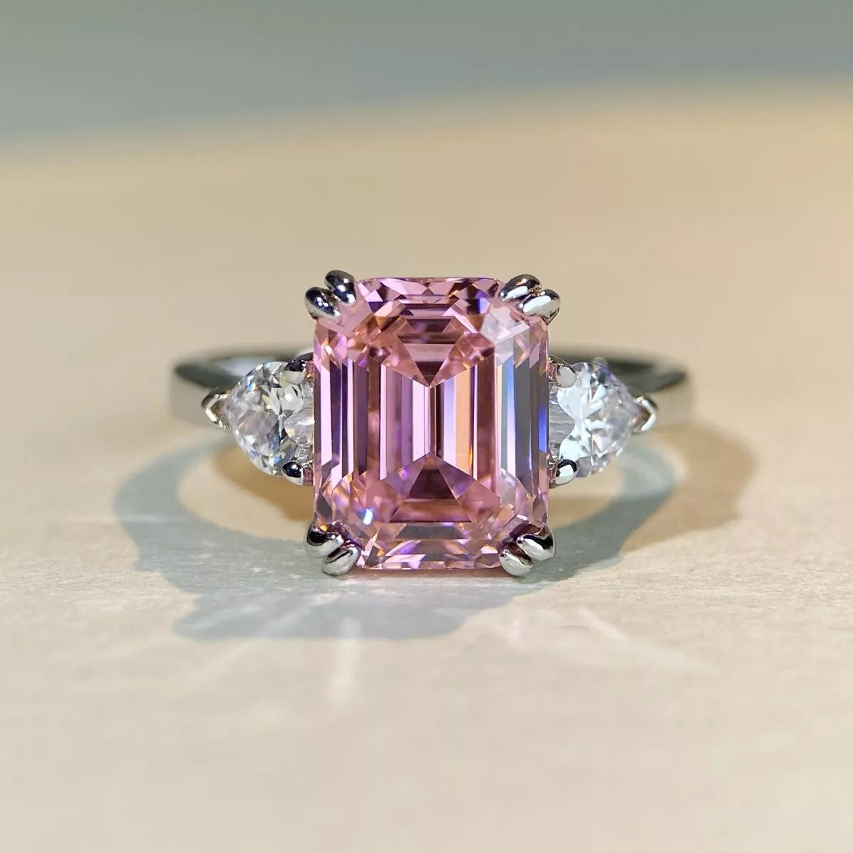 Pink emerald-cut center stone ring with clear side stones on a light surface