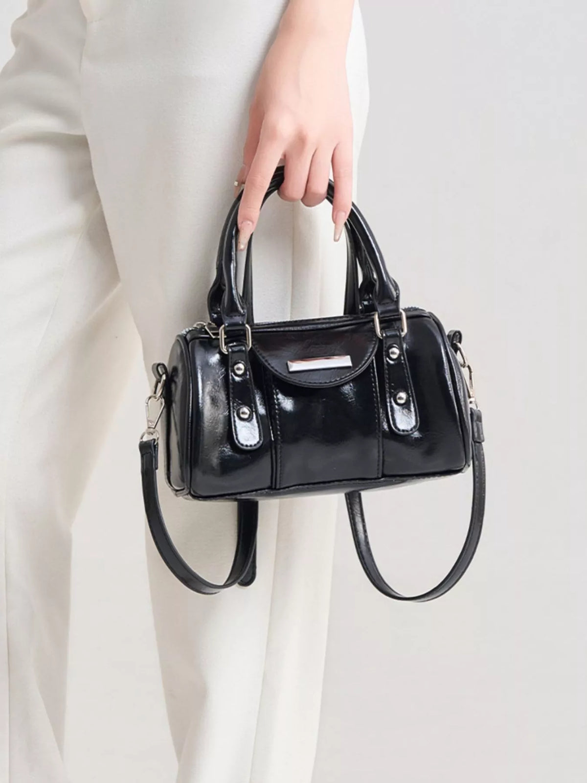 Front view of the glossy black mini Boston bag held by its top handles, with silver-tone hardware.