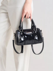 Front view of the glossy black mini Boston bag held by its top handles, with silver-tone hardware.