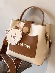 Ivory mini bucket crossbody bag with brown front pocket and bear-face charm