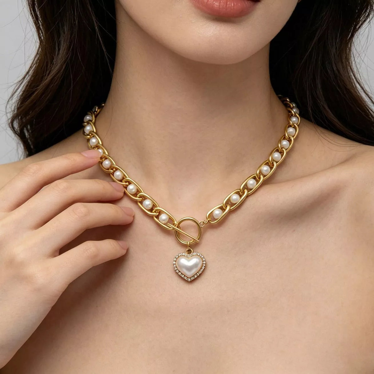 Chunky gold-tone pearl chain necklace with heart pendant, worn at the neck