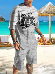Man wearing gray brick-print shirt and shorts with bold black text on a beach