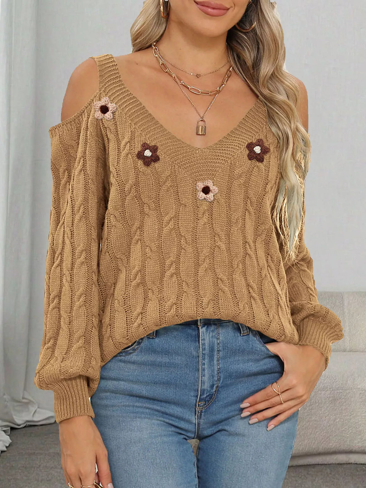 Tan cold-shoulder cable-knit sweater with floral appliqués worn with jeans