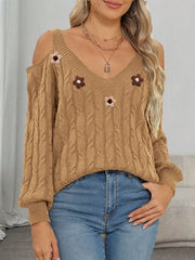 Tan cold-shoulder cable-knit sweater with floral appliqués worn with jeans